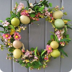 Easter wreath with pastel eggs, pink flowers, and green leaves hanging on a gray wooden door.