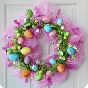 Easter wreath with pink tulle, green foliage, and colorful speckled eggs, hanging on a white door.