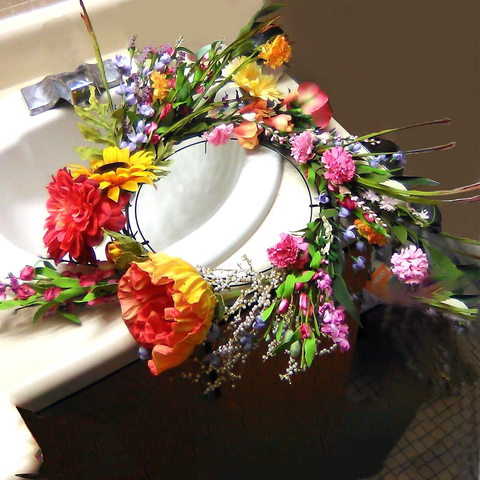 Round wire wreath frame decorated with colorful artificial flowers and greenery, resting on a sink.