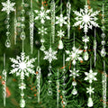 Assortment of clear acrylic snowflake, icicle, and drop ornaments hanging against a blurred green Christmas tree background.