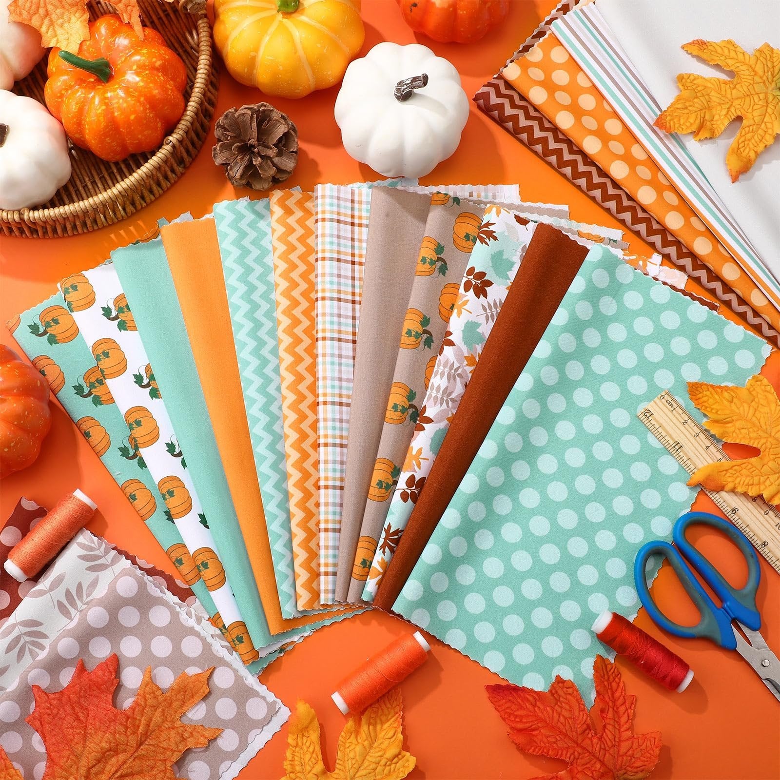 Fall fabric squares with pumpkin and maple leaf prints, arranged with decorative pumpkins, scissors, thread, and a ruler.