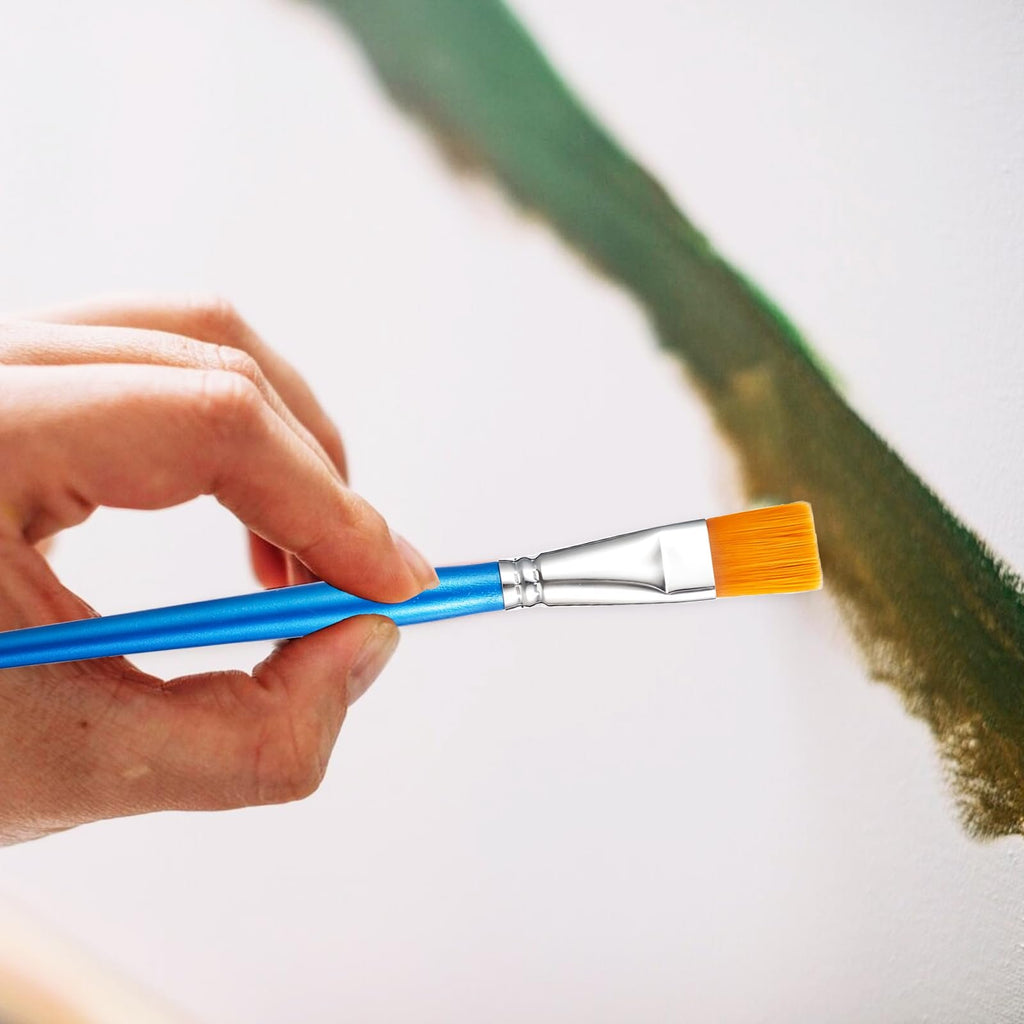 Hand holding a blue-handled flat paint brush with orange bristles, applying green paint to a canvas.