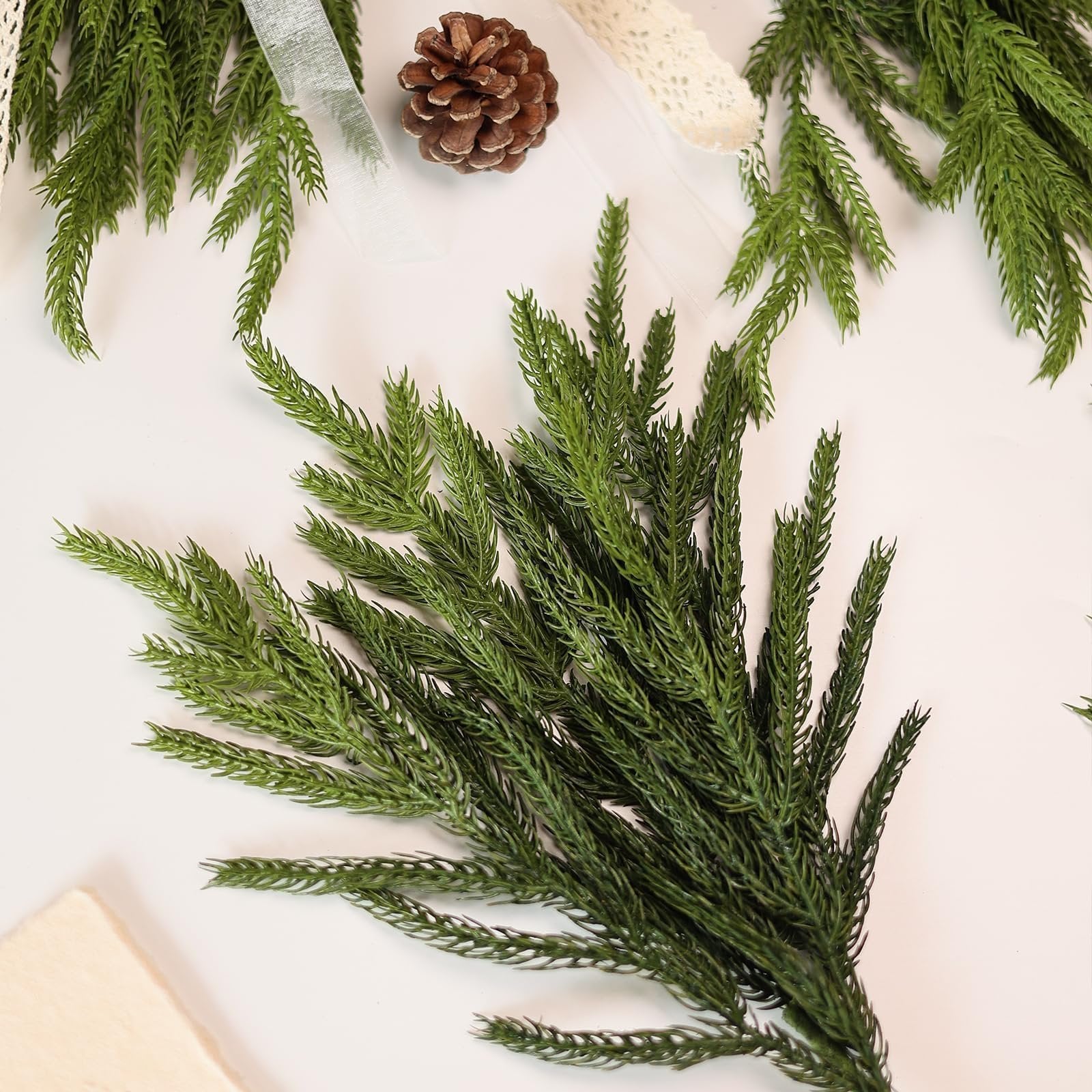 Artificial Norfolk pine branches with a pine cone and lace ribbon on a white background