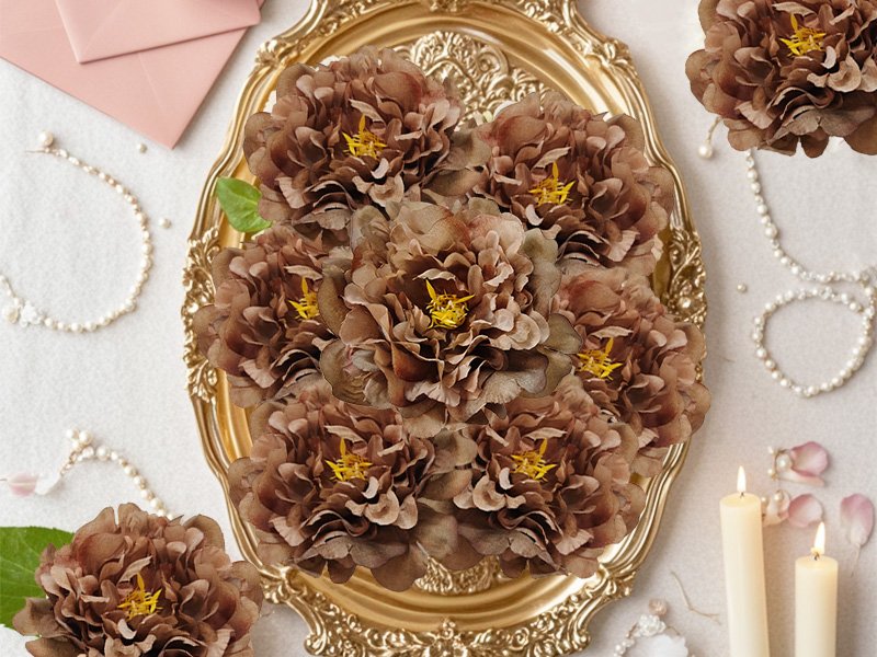 Brown artificial peony flower heads arranged on a gold ornate tray with pearls and candles