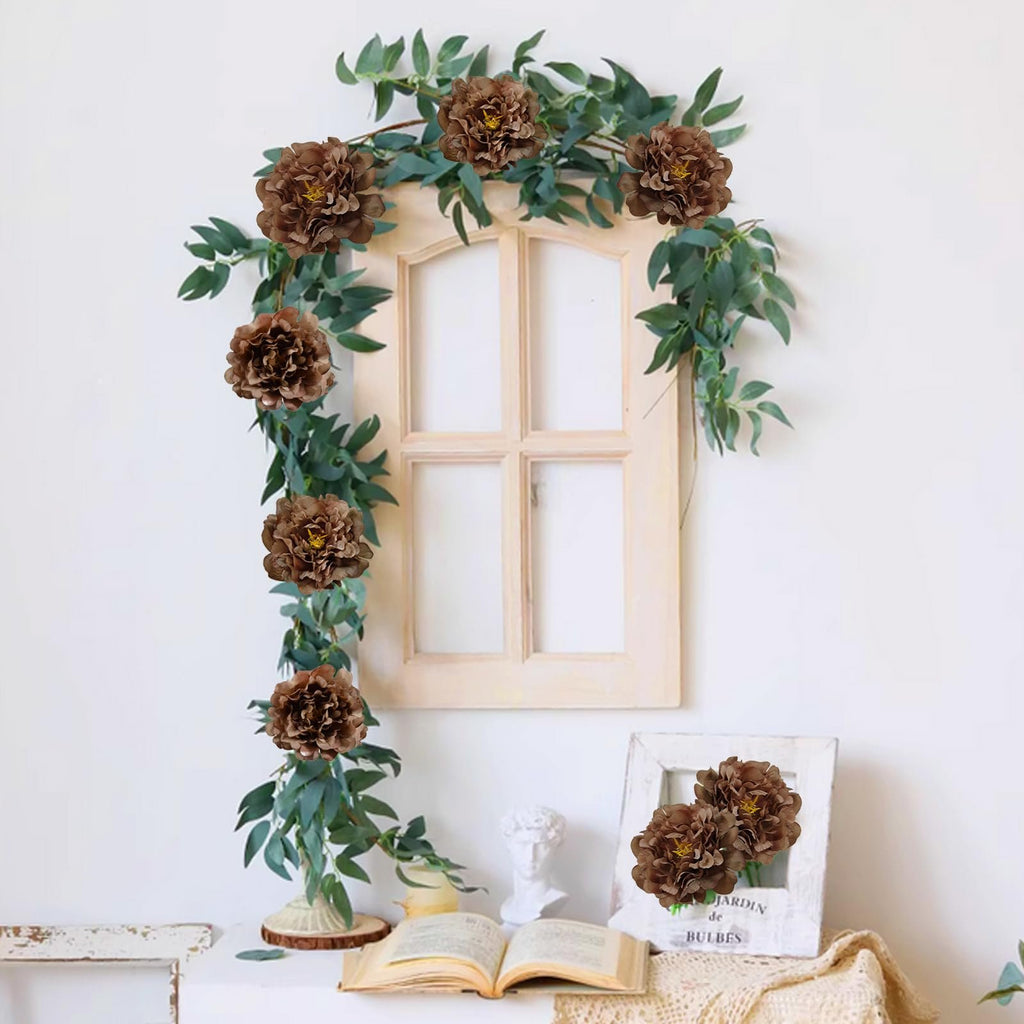 Artificial coffee-colored peony flowers with green eucalyptus garland draped over a decorative window frame.