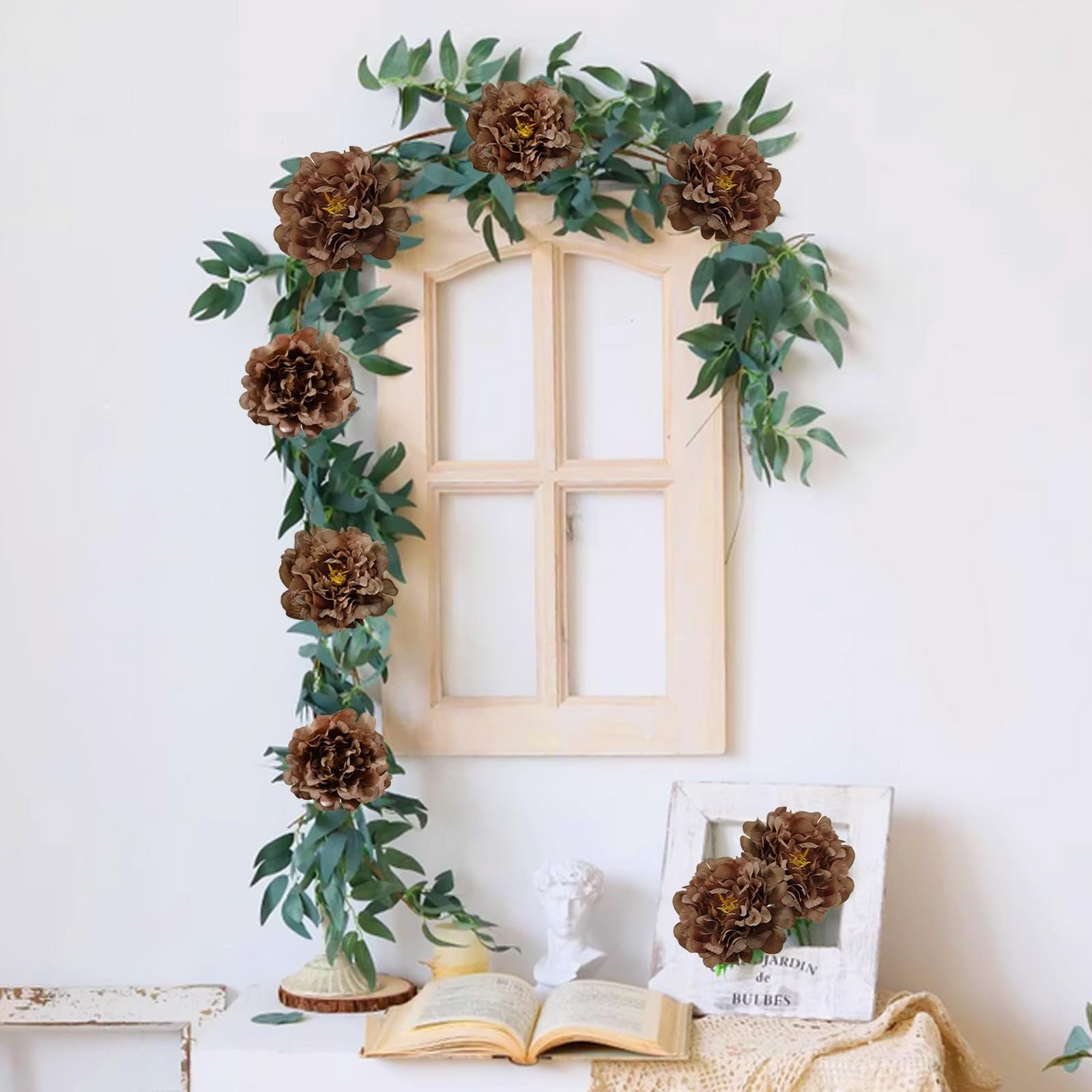 Artificial coffee-colored peony flowers with green eucalyptus garland draped over a decorative window frame.