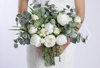 Person holding a bouquet of white peonies and dried eucalyptus stems with green accents