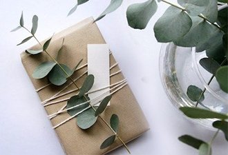 Wrapped gift with twine and eucalyptus sprigs, next to a glass vase with water.