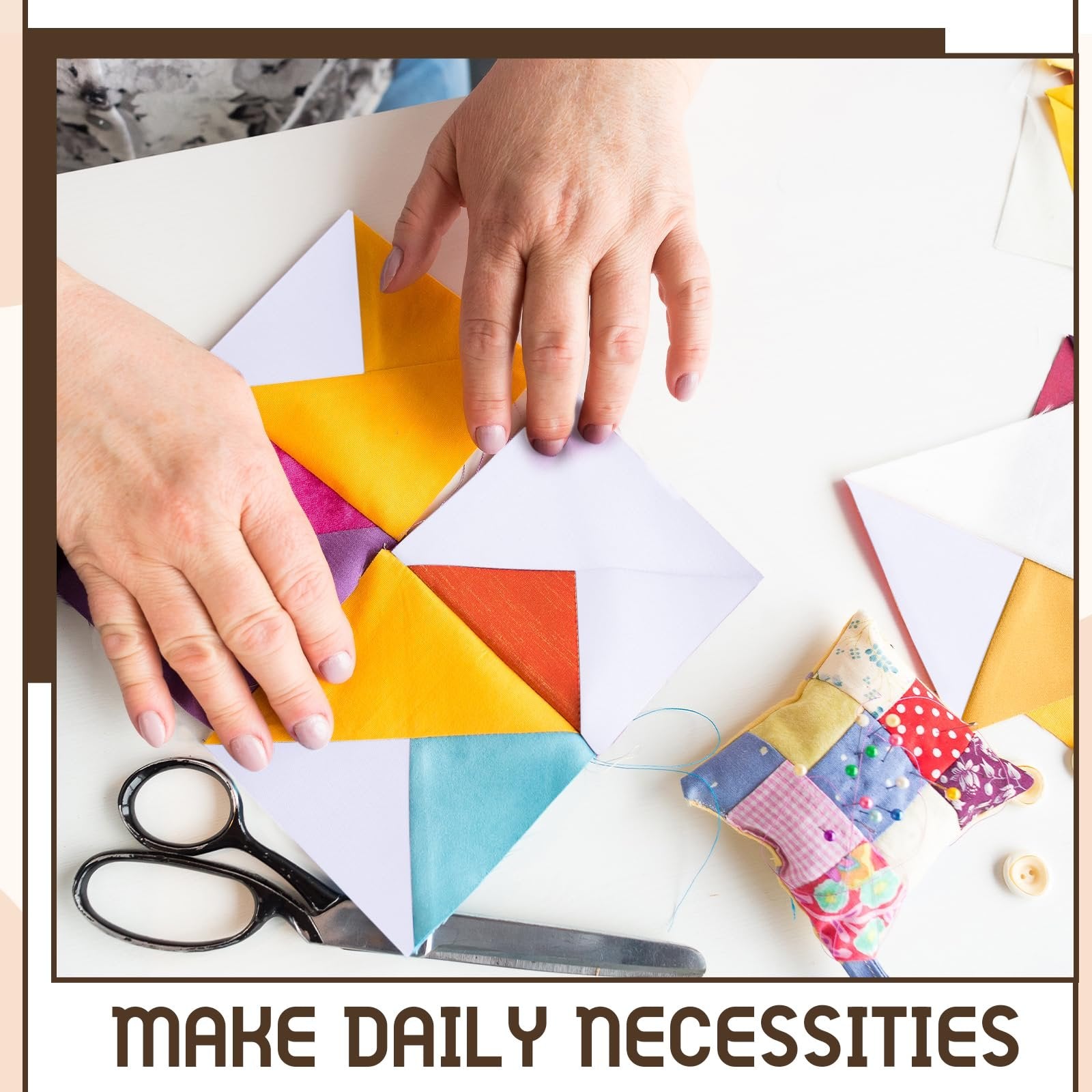 Hands arranging colorful fabric squares into a quilt block pattern on a white surface with scissors and a pincushion.