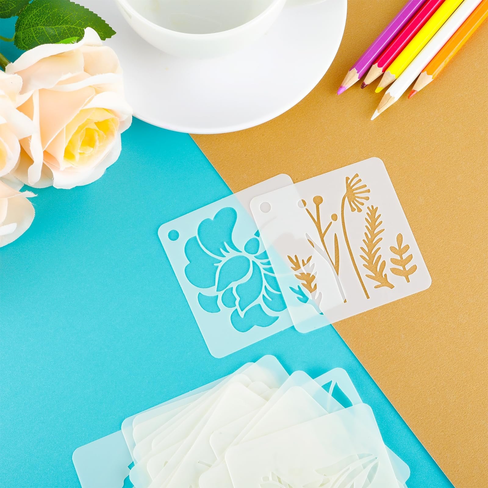 Stack of flower stencils with floral designs, next to colored pencils and artificial roses.