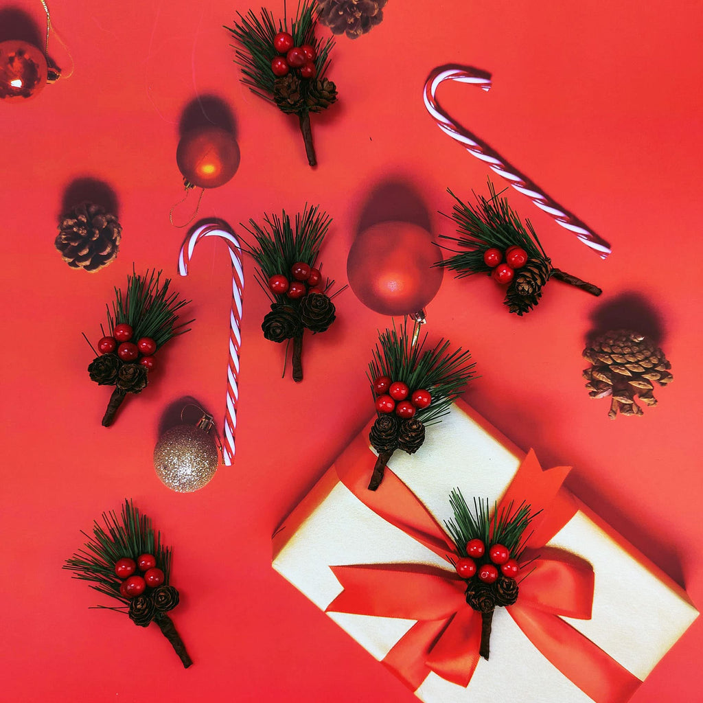 Christmas pine picks with red berries and pinecones arranged with candy canes and ornaments on a red background with a gift box