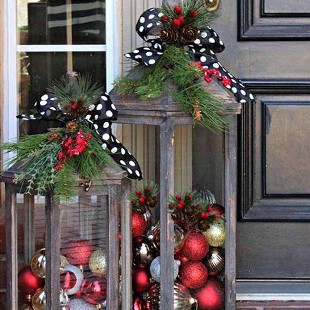 Two wooden lanterns decorated with artificial pine picks, red berries, pinecones, and black and white polka dot bows, filled with Christmas ornaments.