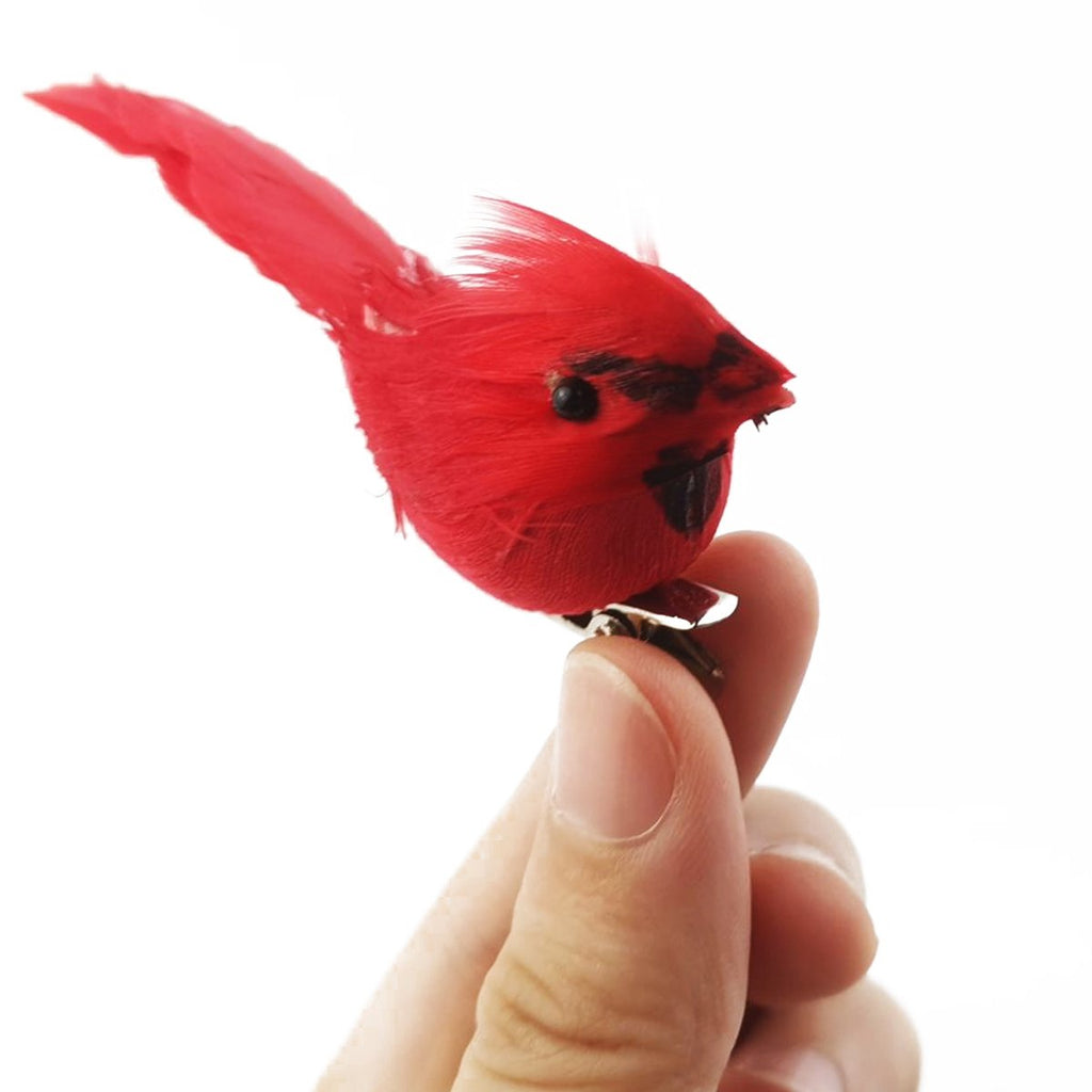 Close-up of a red cardinal ornament with a metal clip held by a finger against a white background.