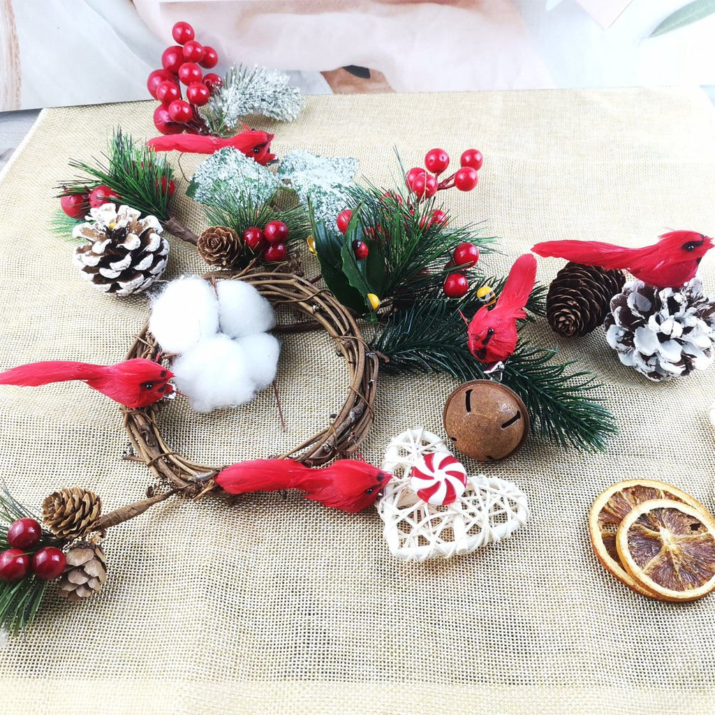 Christmas cardinal ornaments, pinecones, berries, and dried oranges arranged on a burlap surface.