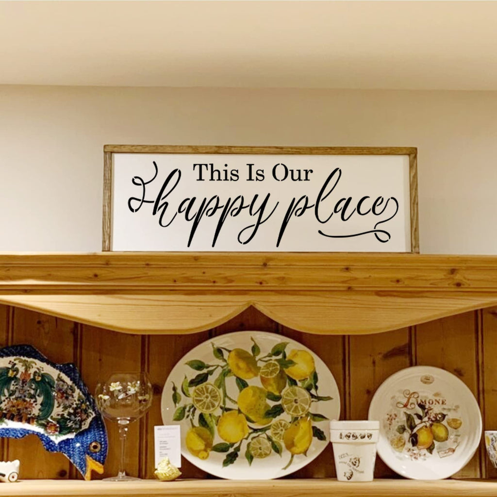 Wooden framed sign with black text 'This Is Our happy place' displayed on a shelf with decorative plates.