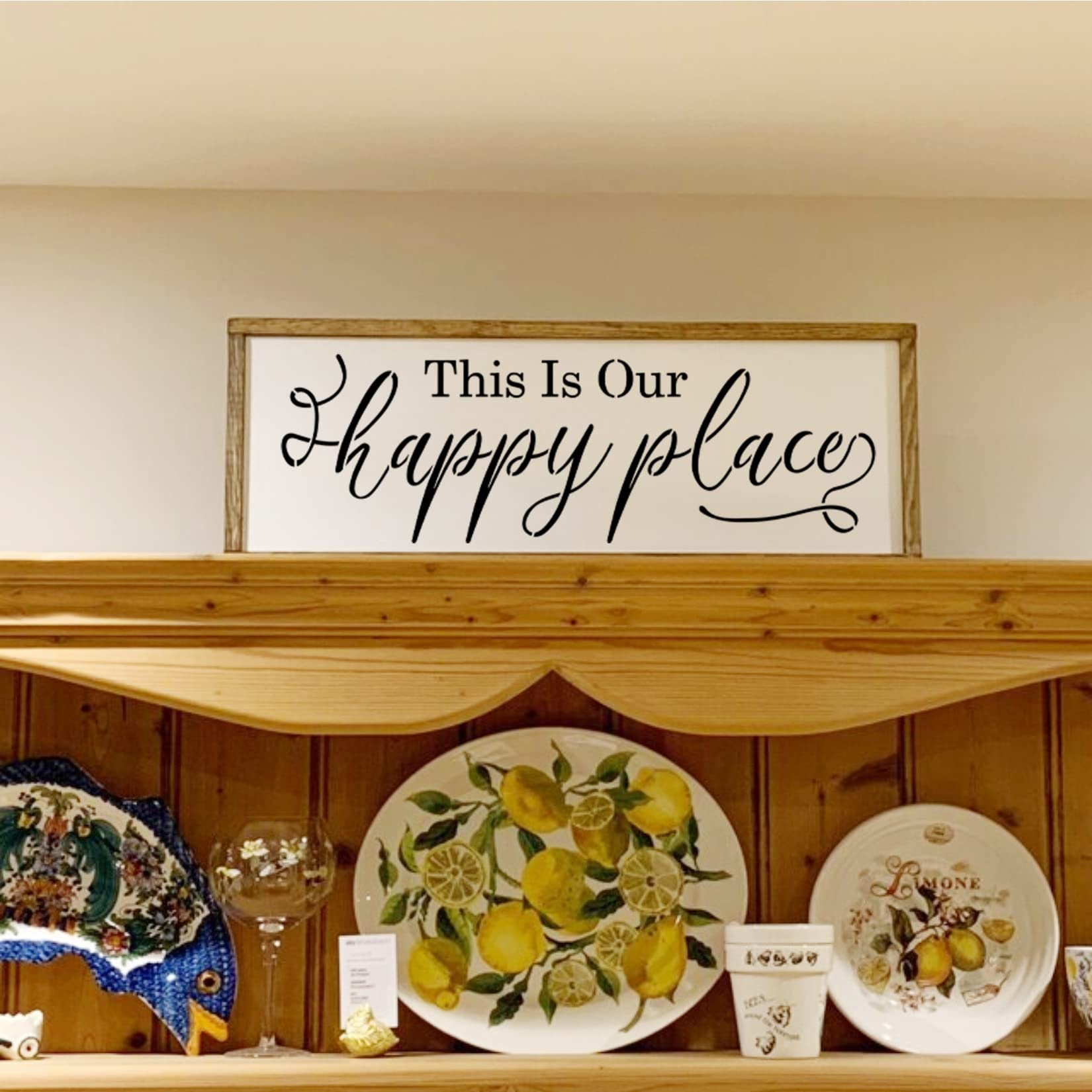Wooden framed sign with black text 'This Is Our happy place' displayed on a shelf with decorative plates.