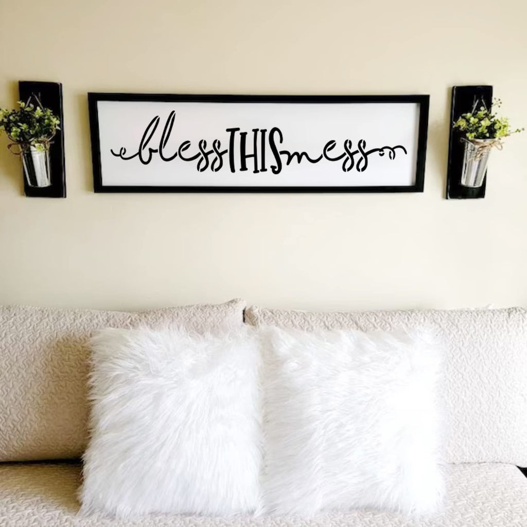 Farmhouse style wall sign with the words "bless THIS mess" in black script and block letters, flanked by two wall-mounted planters with greenery.