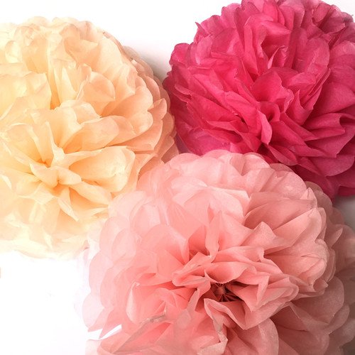 Three tissue paper pom poms in shades of peach, pink, and fuchsia, close-up view.