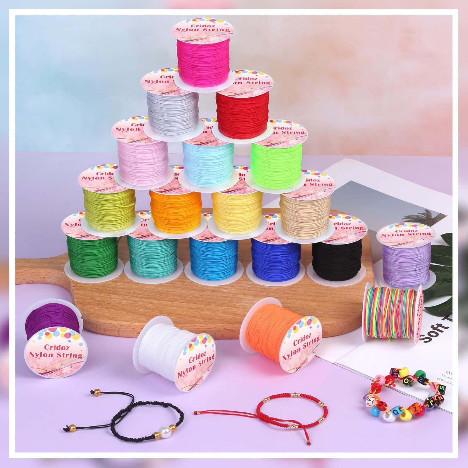 Various spools of colorful nylon knotting cord arranged in a pyramid and scattered, with finished bracelets and a multi-colored spool.