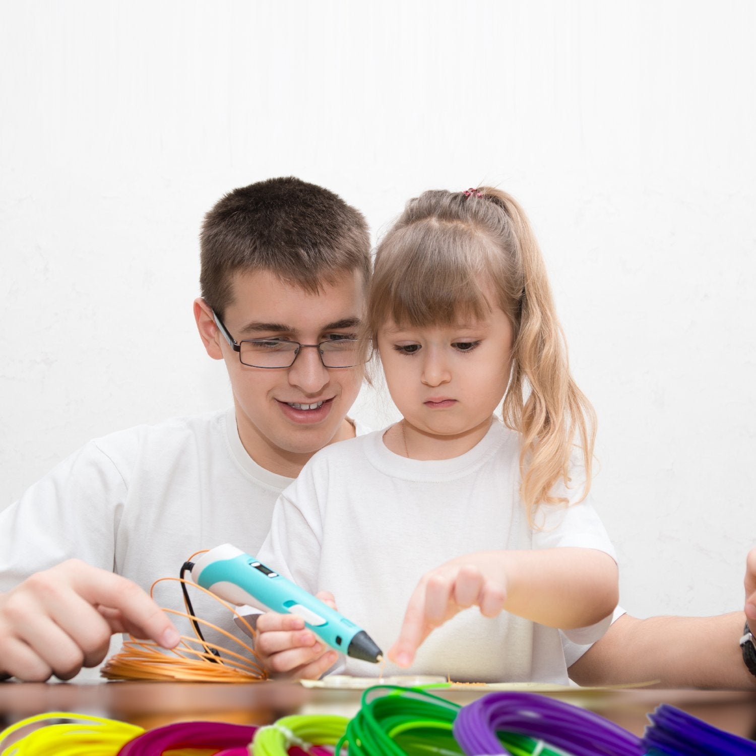 Boy and girl using a 3D pen with colorful filament refills on a table