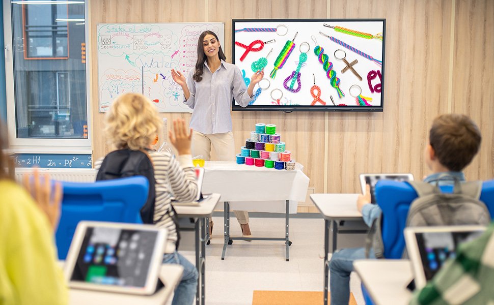 Teacher demonstrating colorful braided lanyards and keychain accessories on a digital display to students in a classroom.
