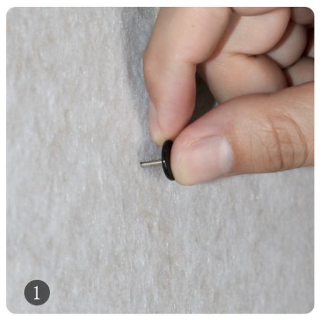 Hand holding a black magnetic pushpin to a textured surface, step 1