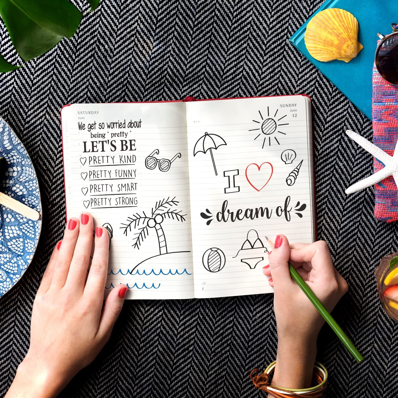 Hands writing in a journal with inspirational quotes and summer doodles, surrounded by decorative items.