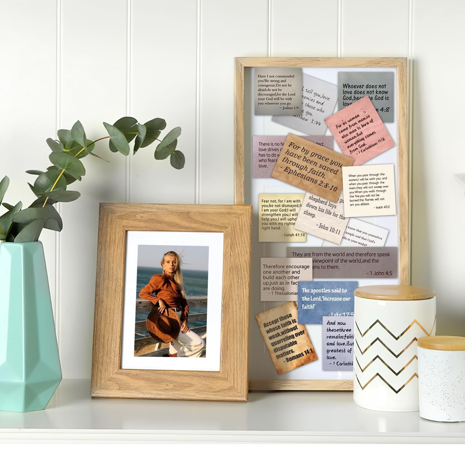A collection of Bible verse stickers arranged on a white wall, with a framed photo of a woman and decorative jars in the foreground.