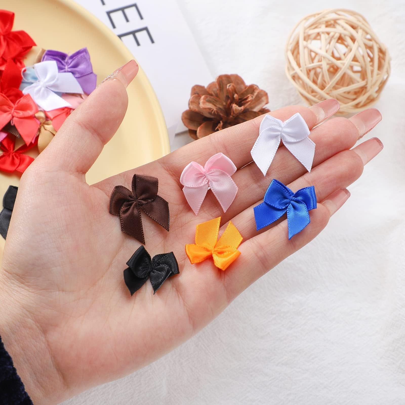 Hand holding assorted mini ribbon bows in white, pink, brown, black, orange, and blue.