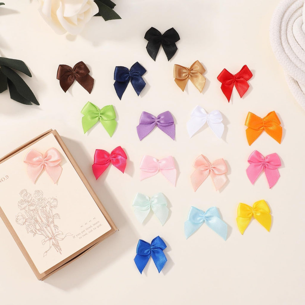 Assortment of 1-inch mini ribbon bows in various colors scattered on a light surface, with a decorative card on the left.