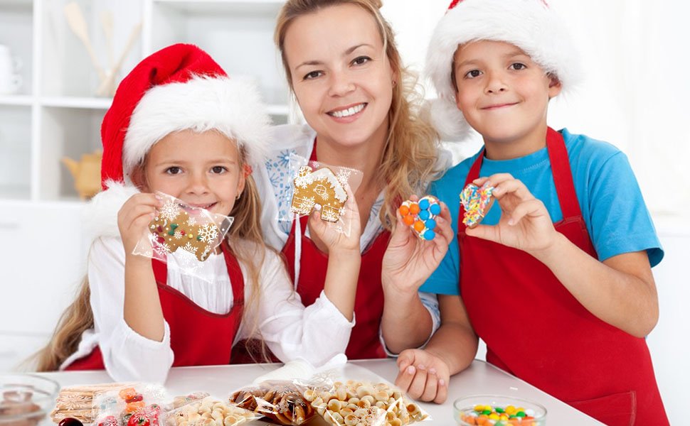 Mother and two children in Santa hats and red aprons holding decorated cookies in clear snowflake-patterned bags.