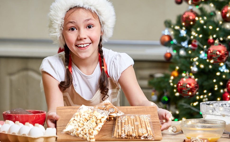 Young girl in Santa hat holding cookie treat bags with snowflakes, Christmas tree in background