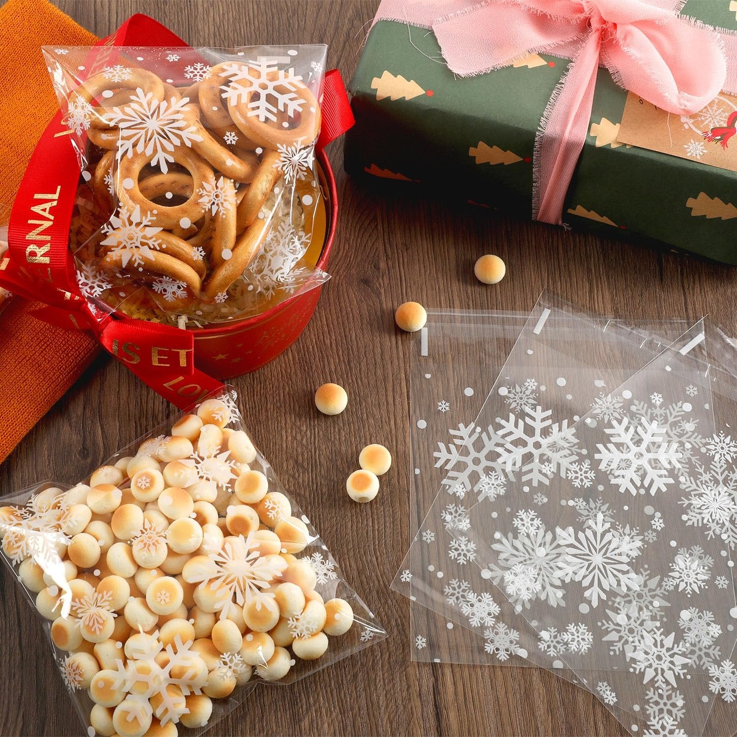 Christmas snowflake cellophane cookie bags filled with small round cookies and pretzel rings, next to a gift-wrapped box.