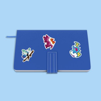 Three vinyl stickers on a blue notebook: a butterfly on a branch, a stylized wing with rainbow colors, and a blue creature with yellow lightning bolts.