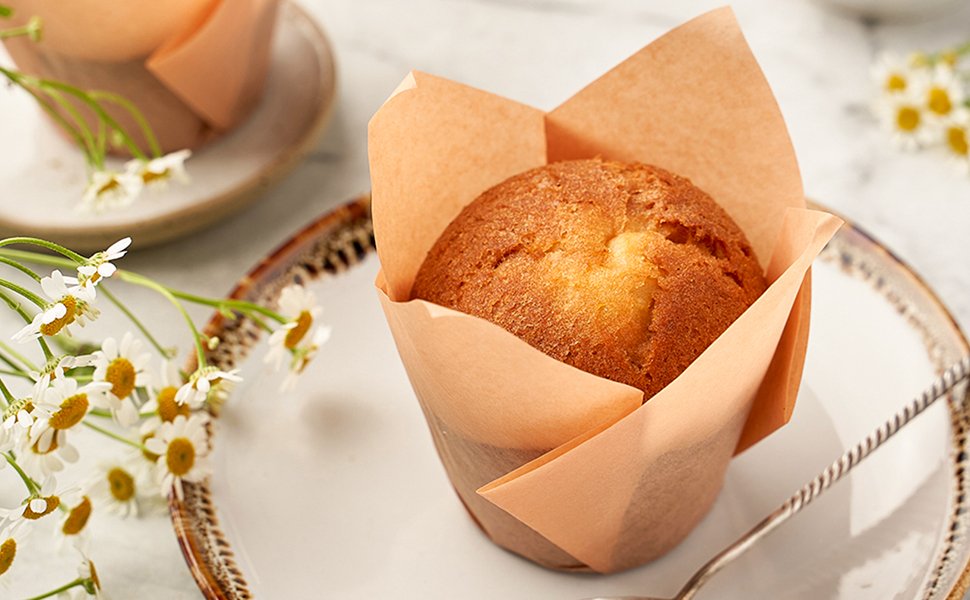 Single baked muffin in a tulip-shaped parchment liner on a plate with daisies and a spoon
