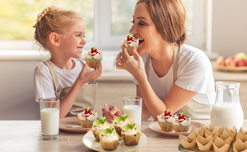Mother and daughter enjoying cupcakes decorated with frosting and berries, with a stack of tulip cupcake liners in the foreground.