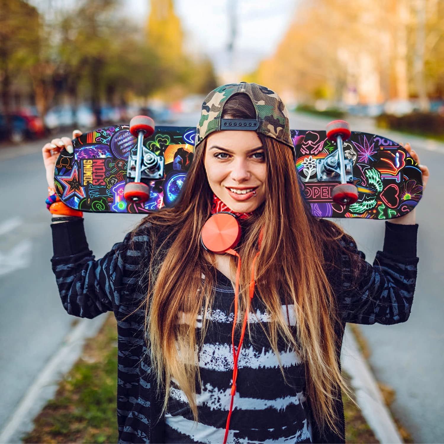 Woman holding a skateboard with colorful neon stickers, outdoors on a street