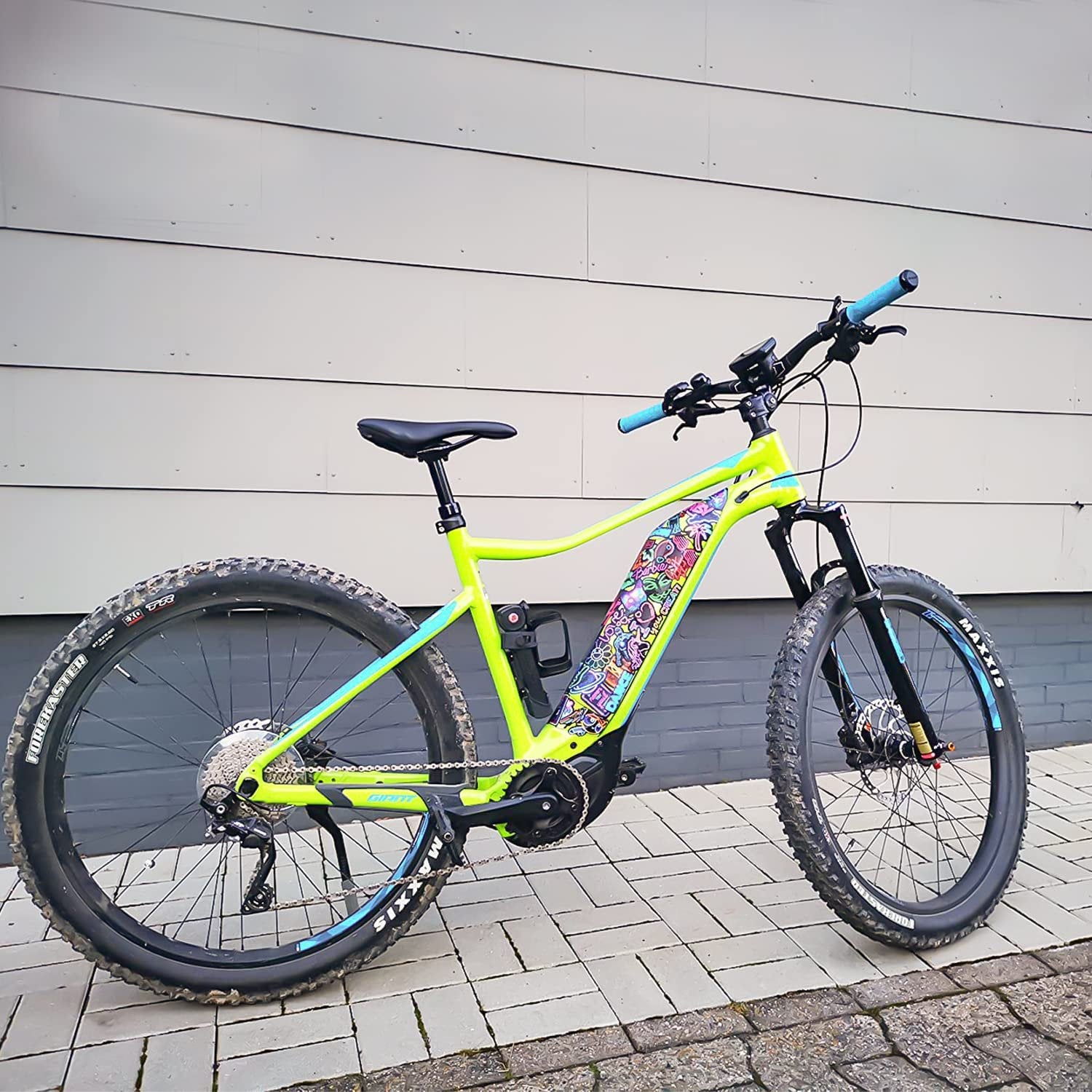 Electric mountain bike with neon stickers on the frame, parked on a paved surface.