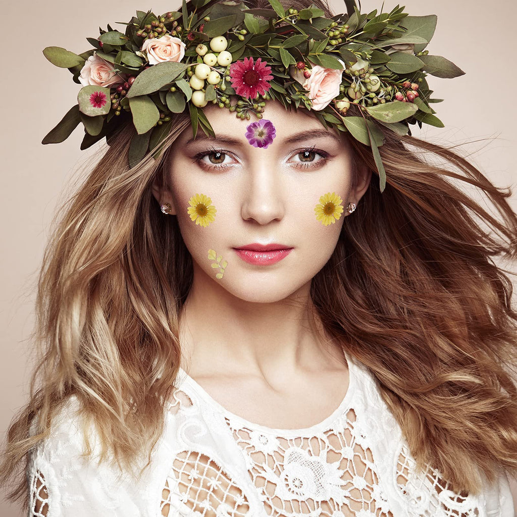 Woman wearing a floral crown and dried flowers on her face, with wavy blonde hair and a white lace top.