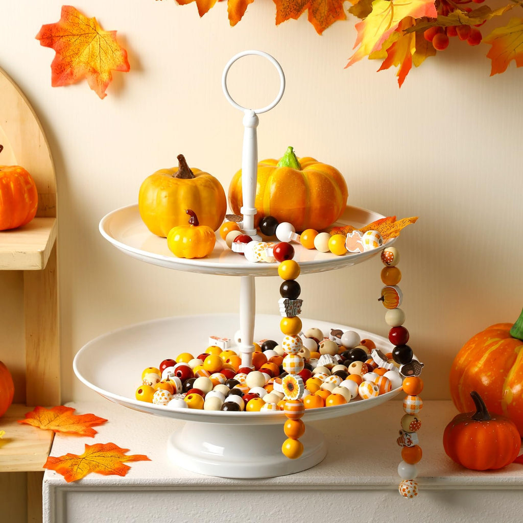 Thanksgiving wooden beads in various fall designs displayed on a two-tiered stand with pumpkins and artificial leaves.