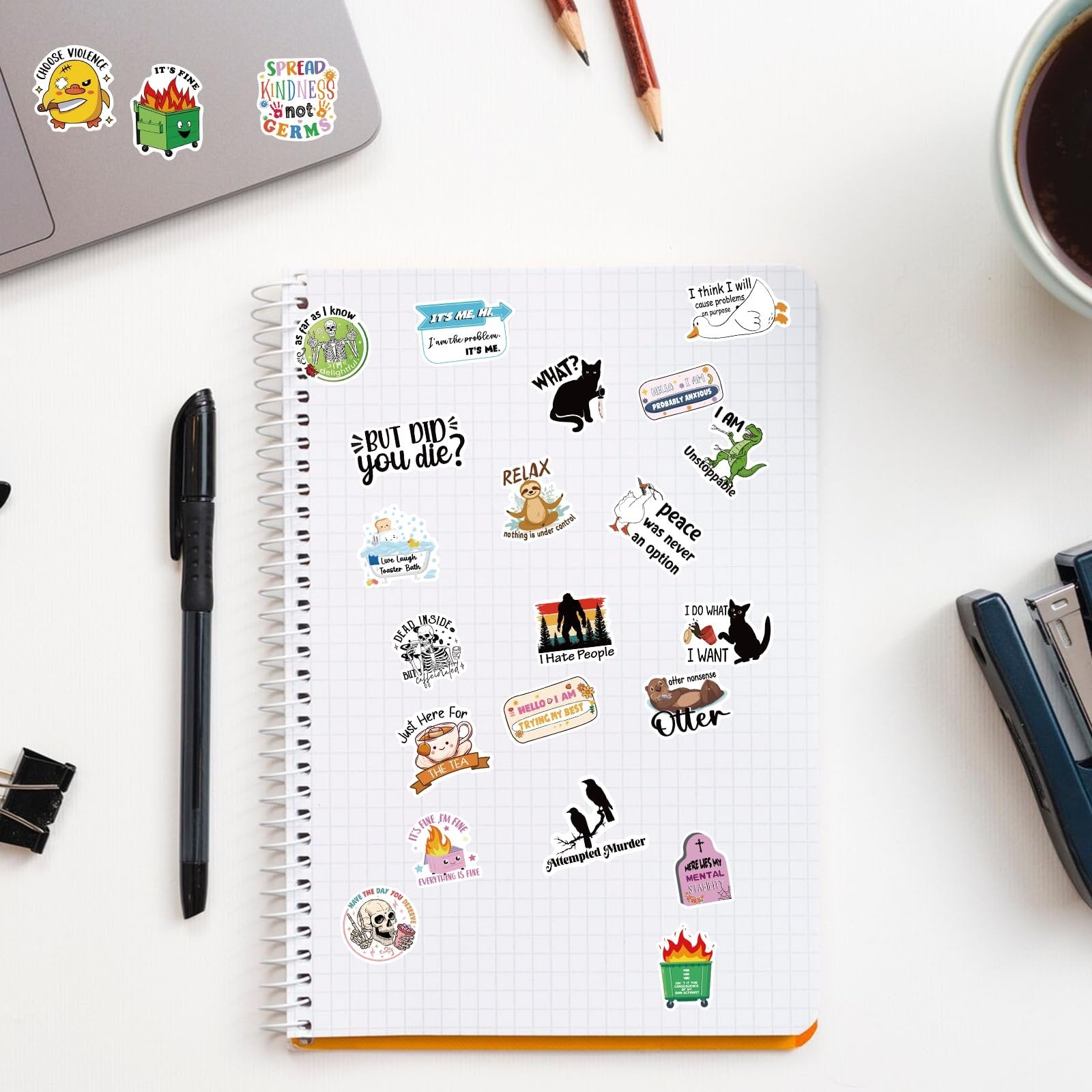 Assortment of funny vinyl stickers scattered on a notebook page and laptop, featuring various designs and text.