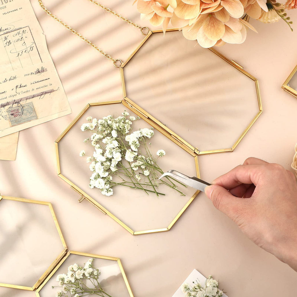 Geometric brass frames with dried baby's breath flowers being arranged with tweezers, flat lay with vintage paper.