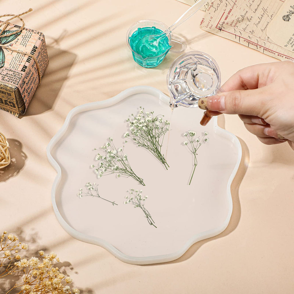 Hand pouring clear liquid into a wavy silicone mold with dried baby's breath flowers inside.