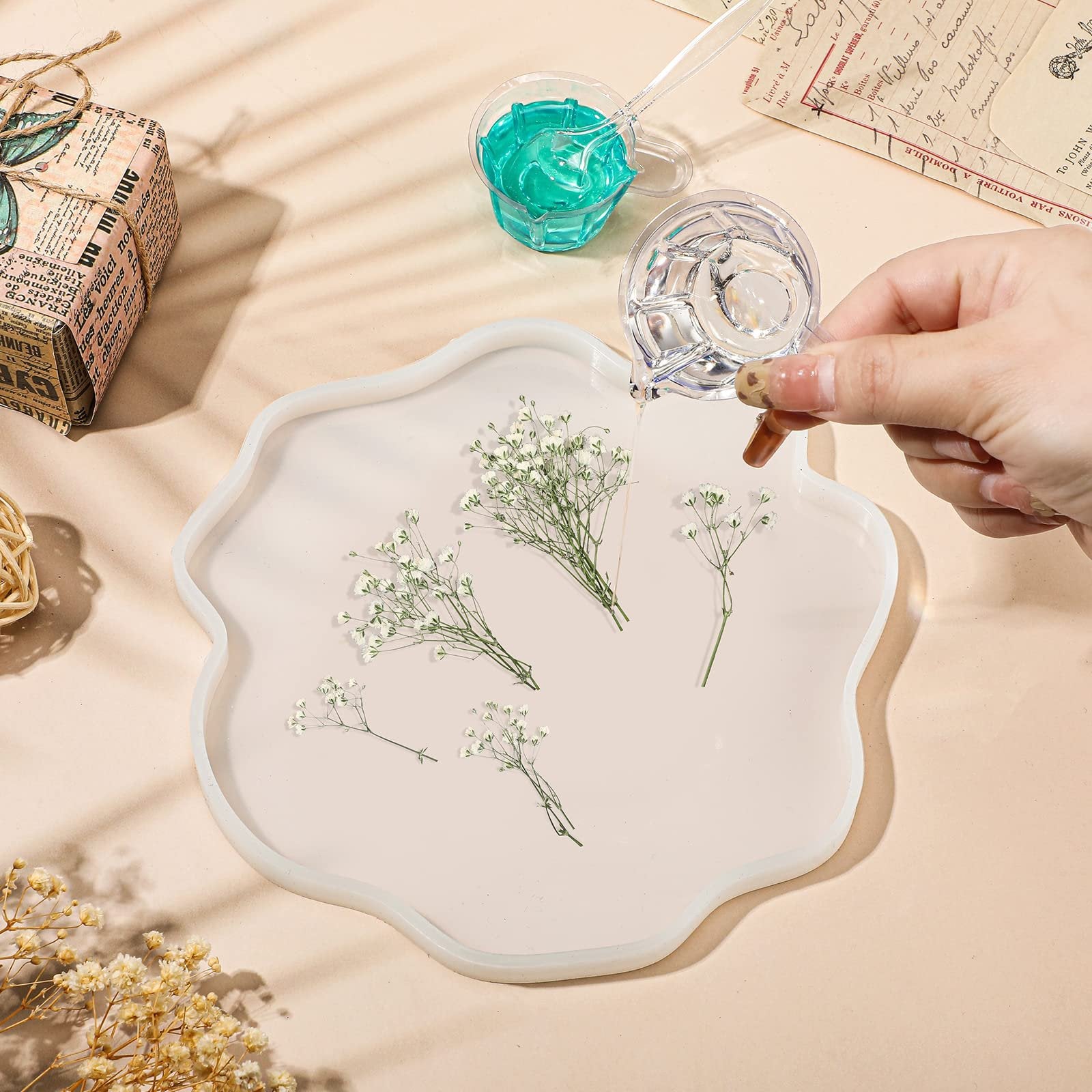 Hand pouring clear liquid into a wavy silicone mold with dried baby's breath flowers inside.