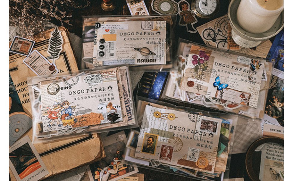 Overhead view of a vintage scrapbooking kit with multiple packs of decorative papers and stickers arranged on a dark, textured surface.