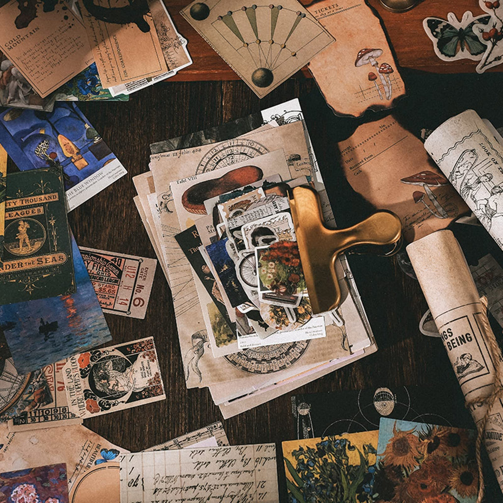 A flat lay of vintage-style scrapbooking ephemera including stickers, papers, and tickets, held together by a gold clip.