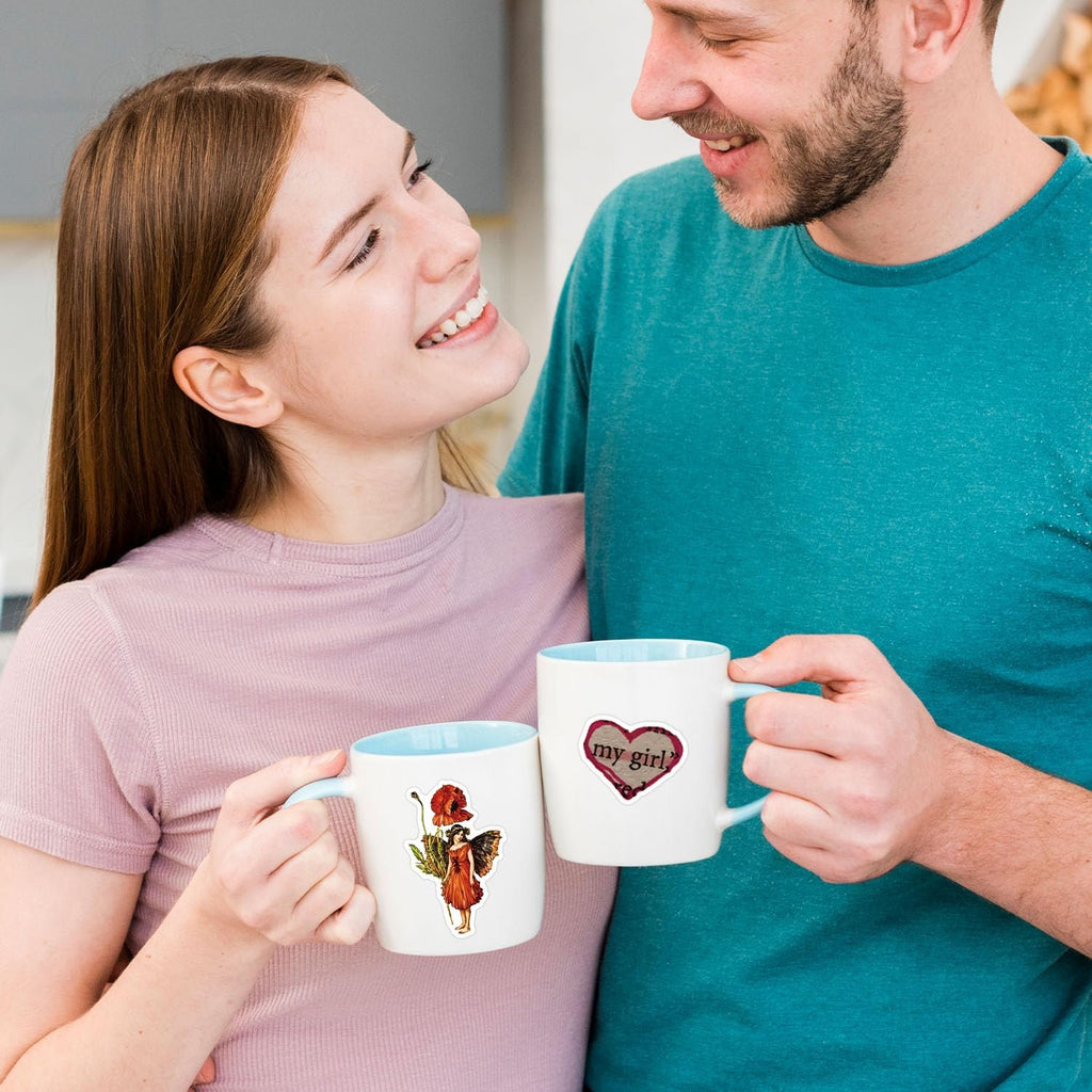 Couple holding mugs with stickers: one with a fairy and poppy, the other with a heart saying 'my girl?'