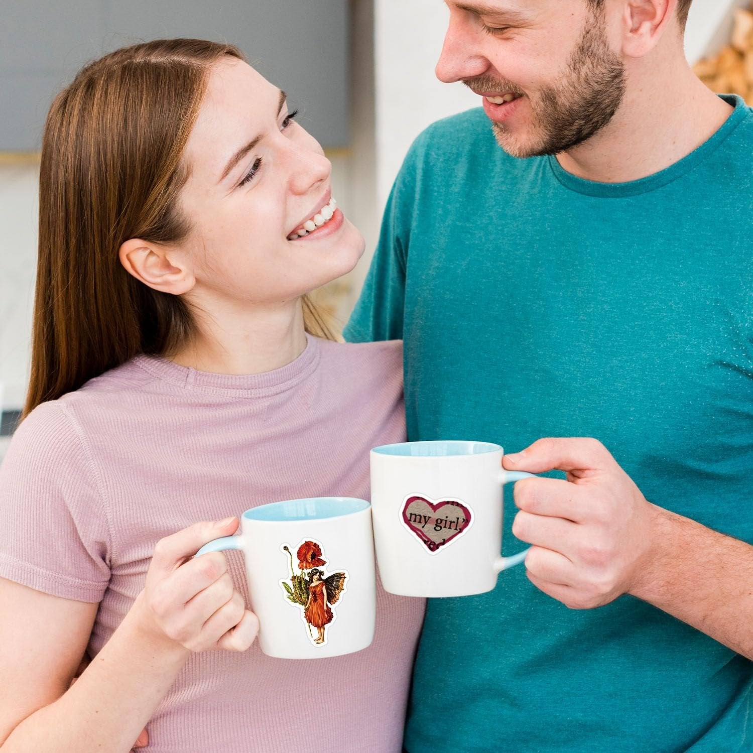 Couple holding mugs with stickers: one with a fairy and poppy, the other with a heart saying 'my girl?'