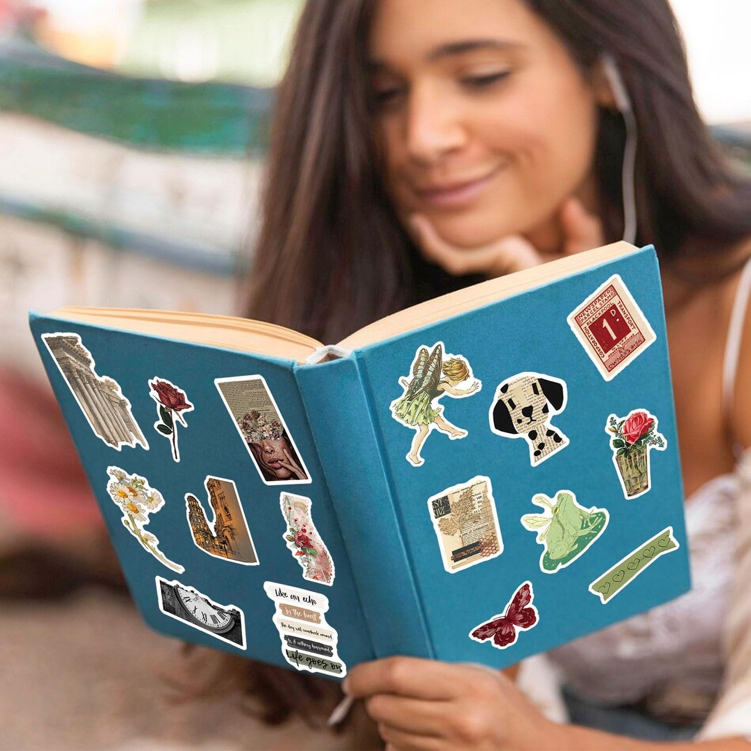 Woman reading a book decorated with vintage vinyl stickers including a fairy, dog, rose, and clock.