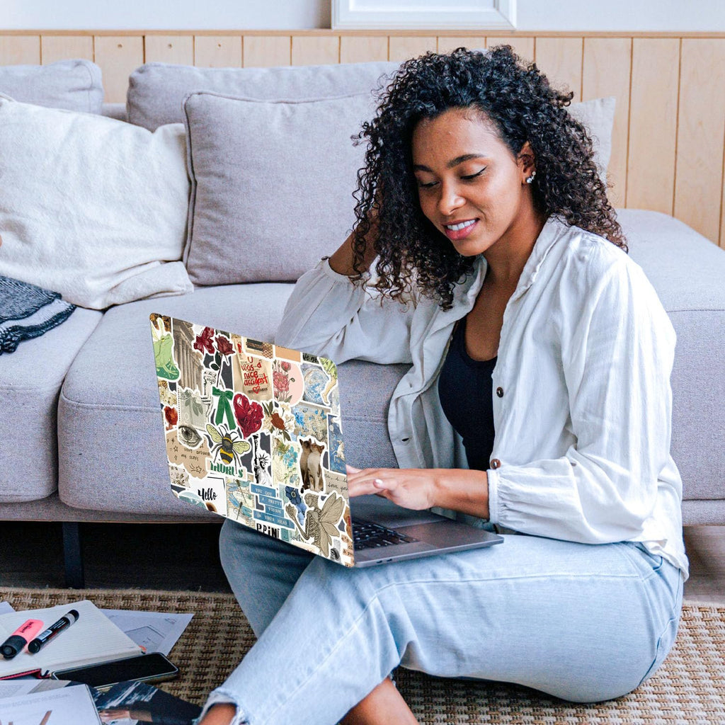 Woman with curly hair sitting on floor using laptop decorated with vintage stickers